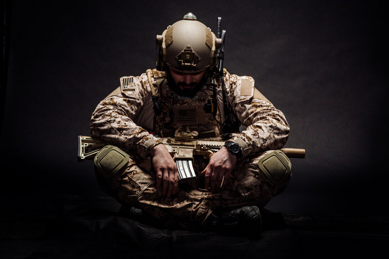 solider sitting cross-legged with his rifle, head bowed